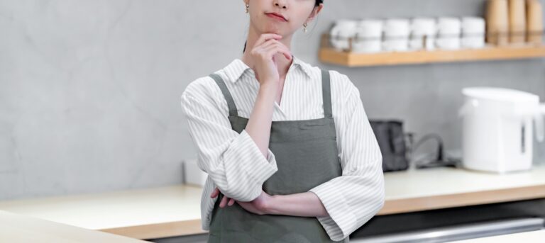 カフェで頭を抱えるエプロンをつけた女性